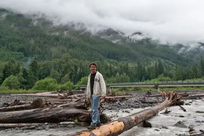 Man standing on a log over the over the Carbon River by the intersection of Fairfax Forest Reserve Rd E (Carbon River Rd) and NF-7810 (Cayada Creek Road) looking North in Mt. Baker-Snoqualmie National Forest, WA (DSC 0613)