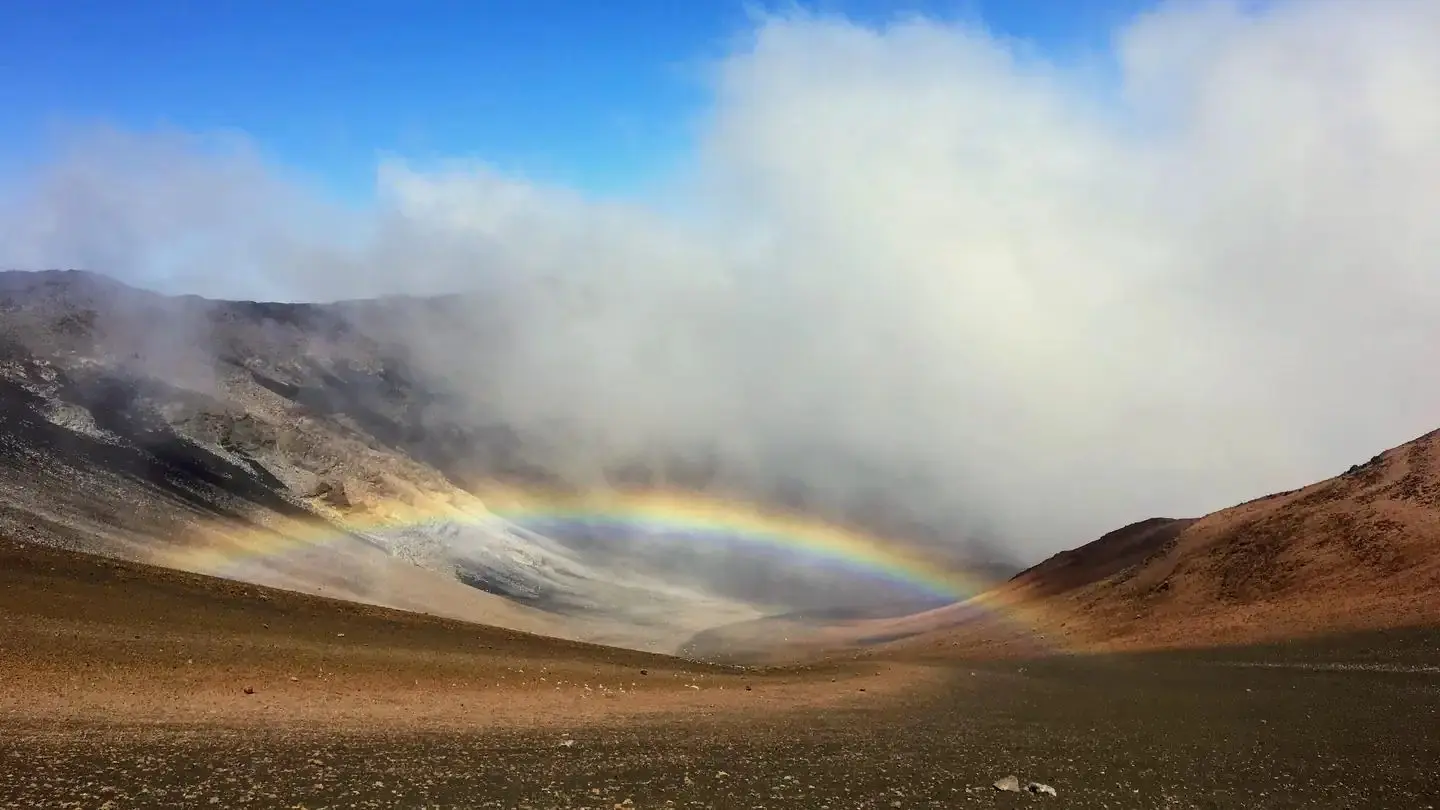 view of crater, orange and black cinder hills with clouds and a low rainbow