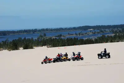 Off road vehicles on flat expanse of sand in front of blue lake ringed by conifer trees.