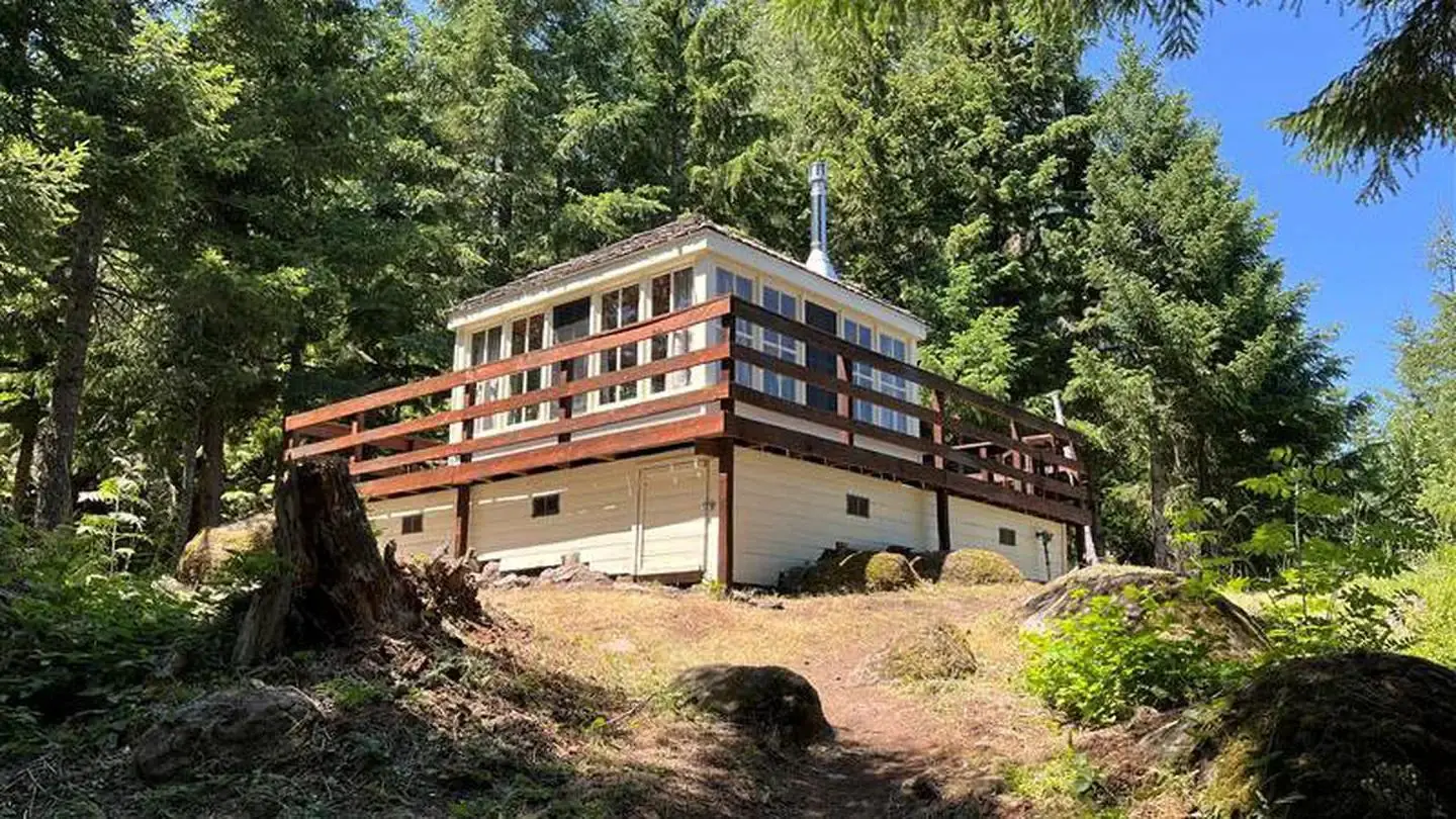 Trail leading to lookout with wraparound deck framed by fir trees, a glimpse of blue sky.