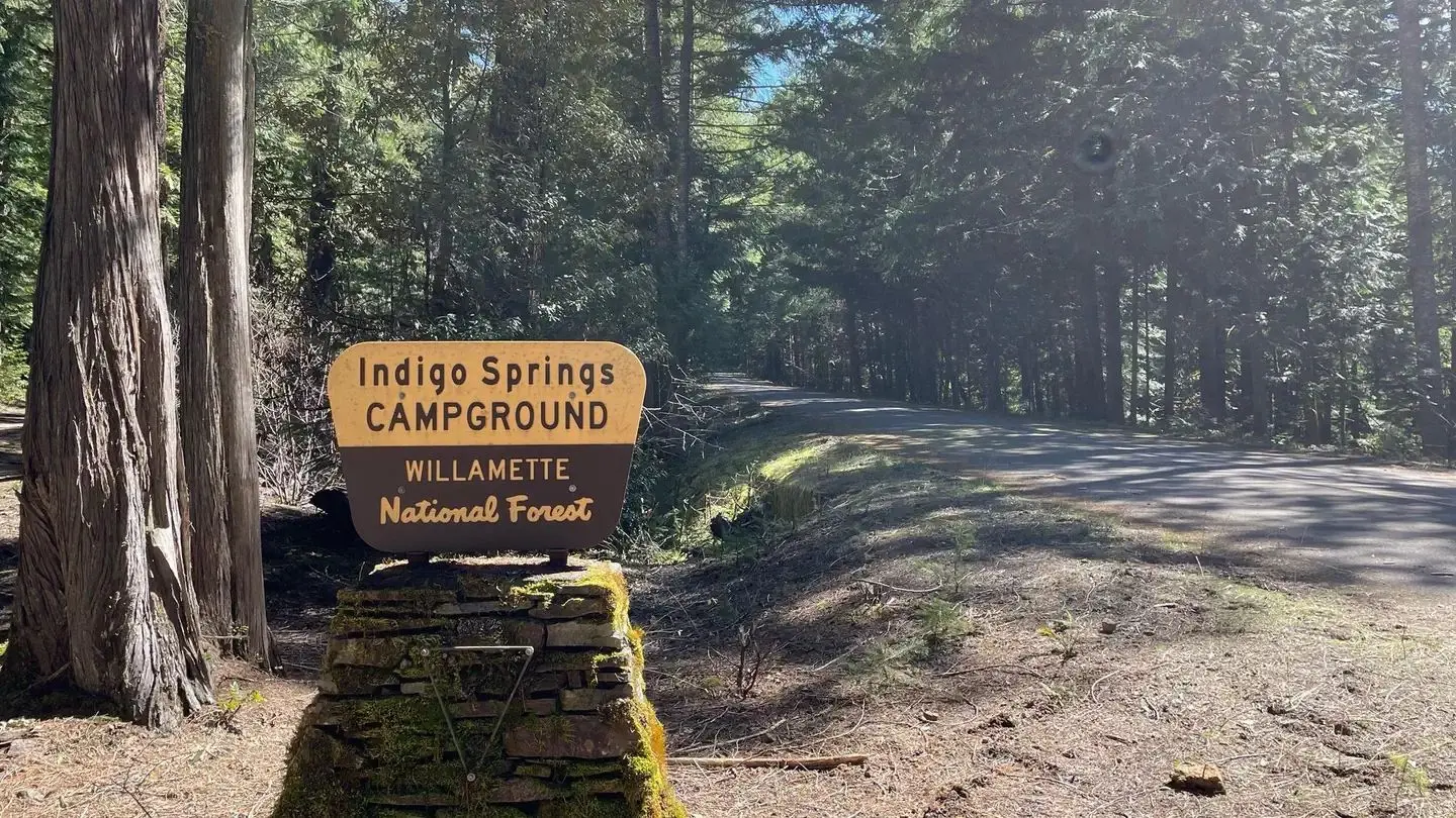 A cream and brown sign on a stone pedestal. The sign reads "Indigo Springs Campground"
