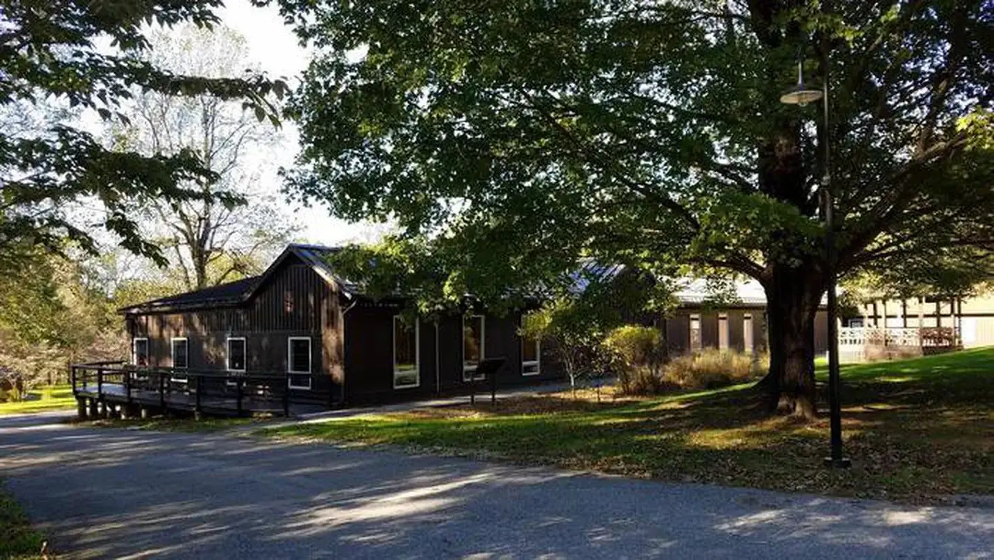 Dining Hall building front entrance view showing wooden gazebo and maple tree.  Side of building has wooden accessibility ramp.