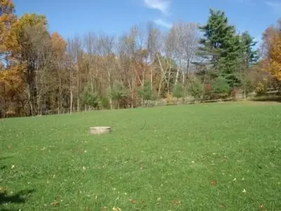 Large outside grass athletic field located behind the dining hall.  Trees showing fall foliage in the distance.