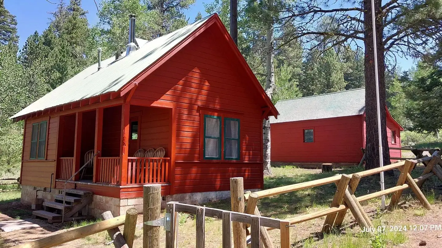 A sunny day illuminates Patterson Guard Station. The bright red color of the Guard Station contrasts the green conifer trees behind it.