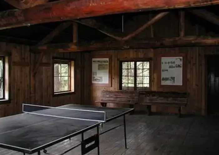 Ping-pong table in dimly lit large room with log rafters and benches.
