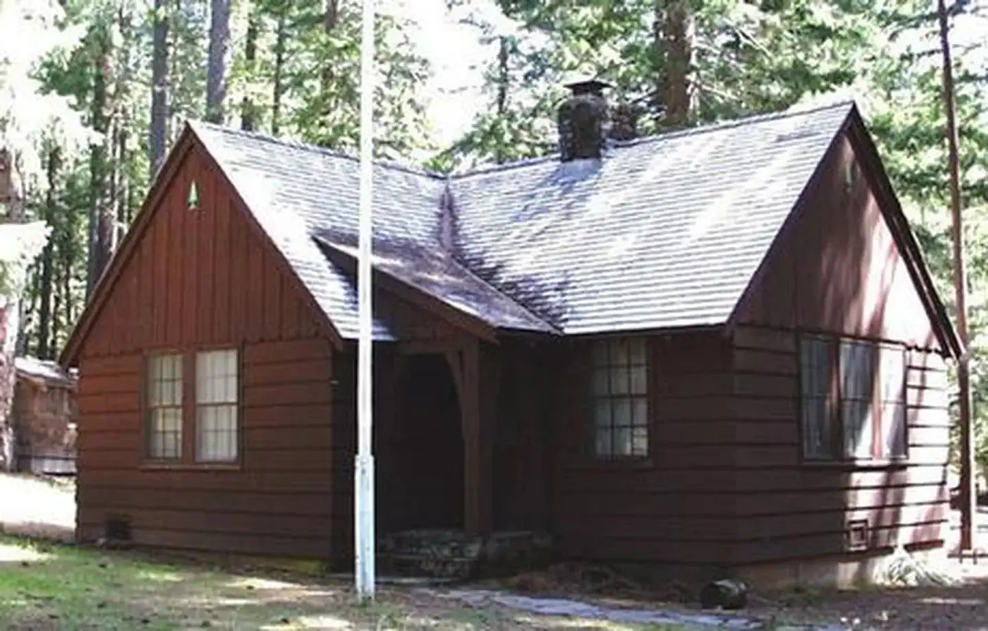 Flag pole in front of L-shaped house in conifer forest.
