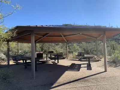 Large covered ramada with 3 picnic tables, benches, a grill and trashcans