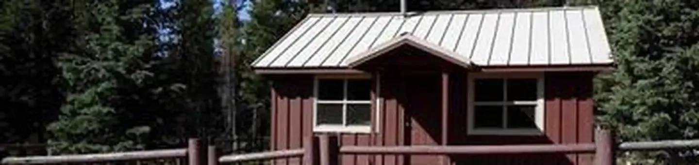 Cabin with red siding in front of conifer forest