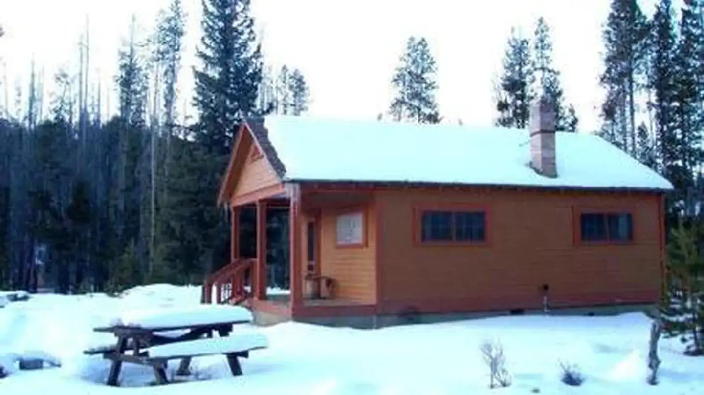 Thick snow covers a wooden cabin and picnic table.