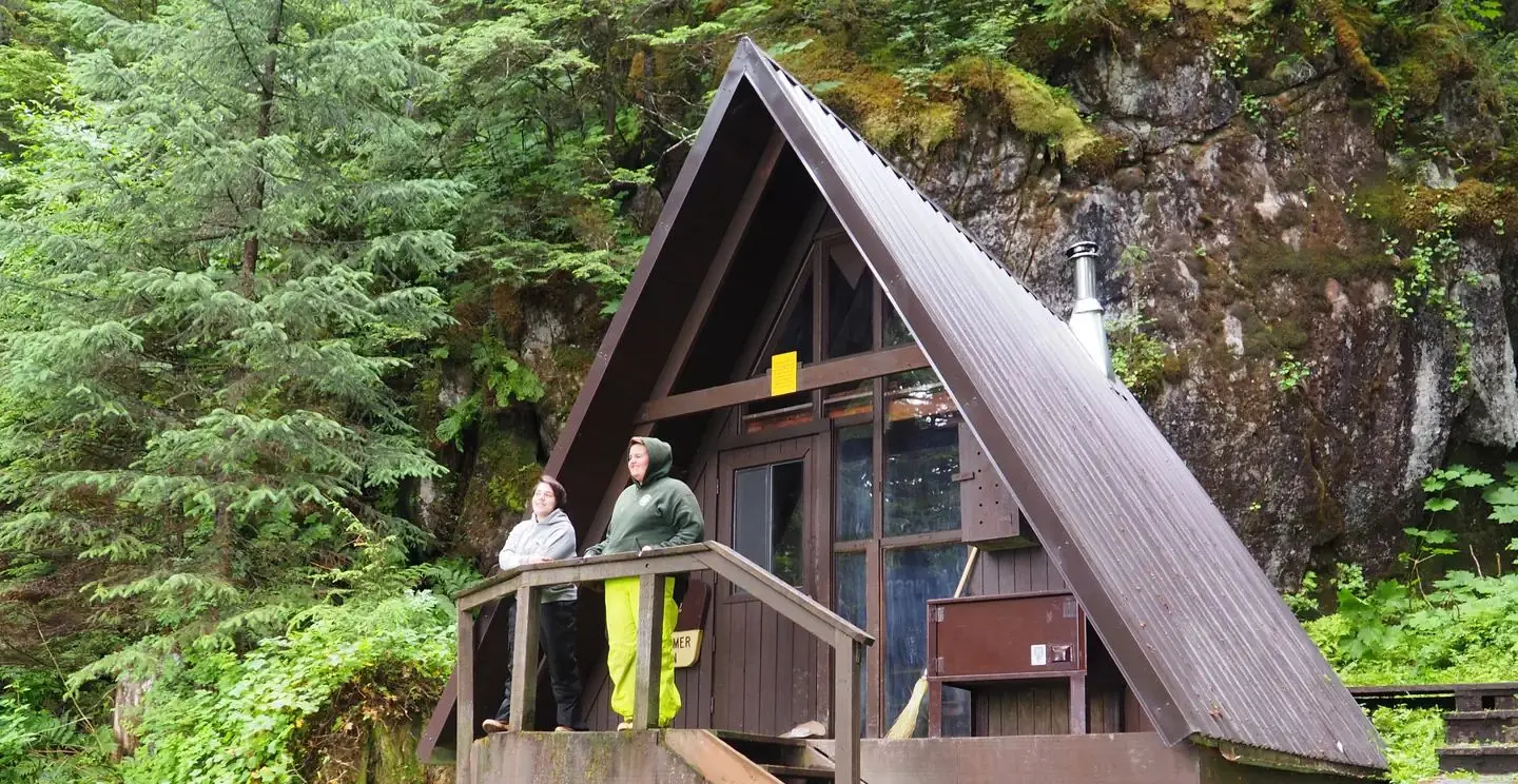 Two people by railing of entrance to Mount Flemer Cabin with trees in background