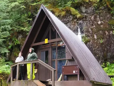 Two people by railing of entrance to Mount Flemer Cabin with trees in background