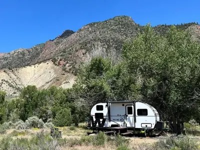 Campsite with recreation trailer, picnic table, fire pit, mountain, trees, and sagebrush.