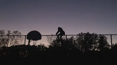 Silhouette of someone scaling a fence at a basketball court