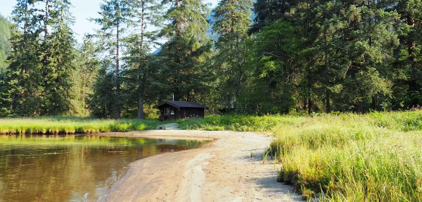 Marten Lake Cabin with trees surrounding it and water in front with a small boat and tall grass