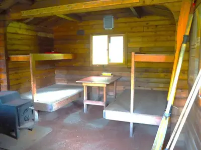 Marten Lake Cabin interior showing 4 wood bunkbeds, small table and stove with oars leaning against wall