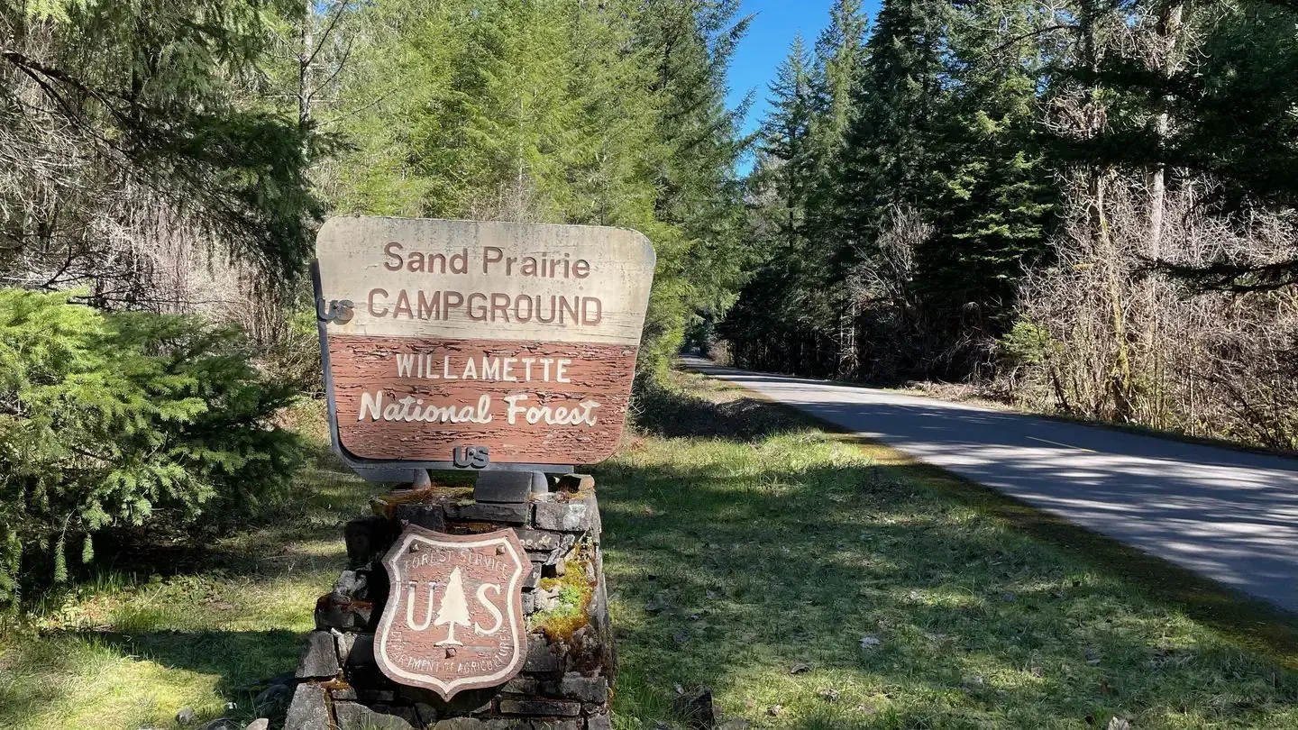 A wooden sign on a stone base. The sign is brown and cream colored and reads "Sand Prairie Campground"