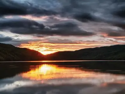 Sun sets behind the mountains looking over a mirror-surfaced lake.