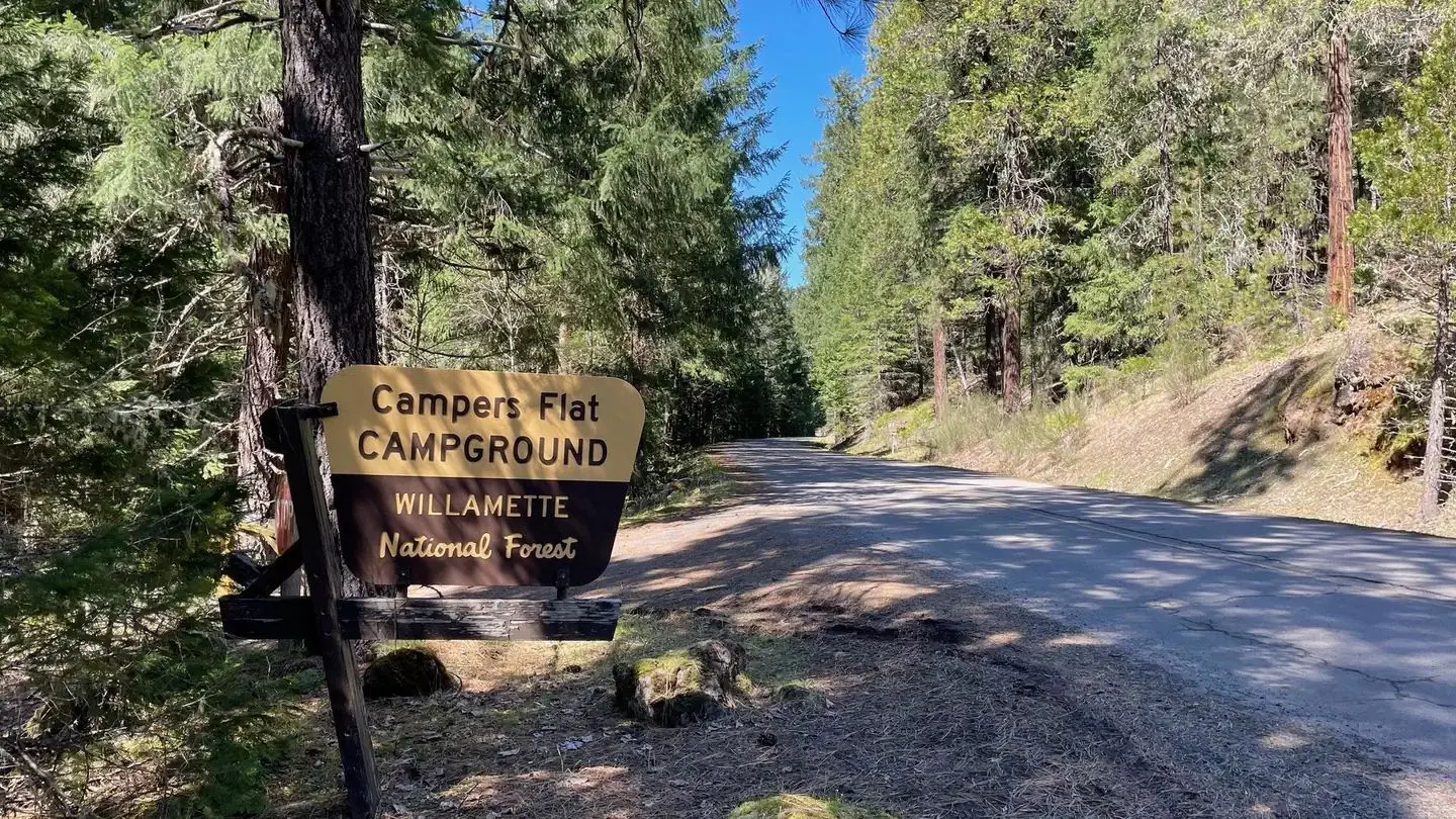 A brown and cream sign on a wooden stand. The sign reads "Campers Flat Campground".