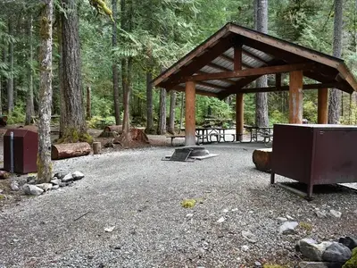 Shelter provided rain and sun protection to several picnic tables located underneath. Campfire ring and food storage lockers in foreground.