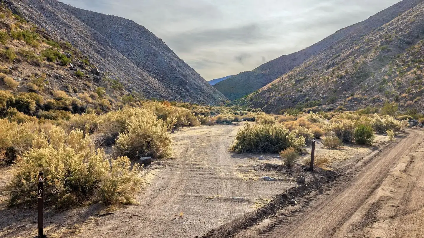 Gravel dirt road with parallel roadside campsite surrounded by mountains.
