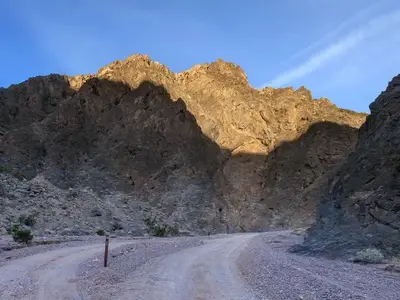 Gravel dirt road with a parallel roadside campsite surrounded by dark canyon walls.