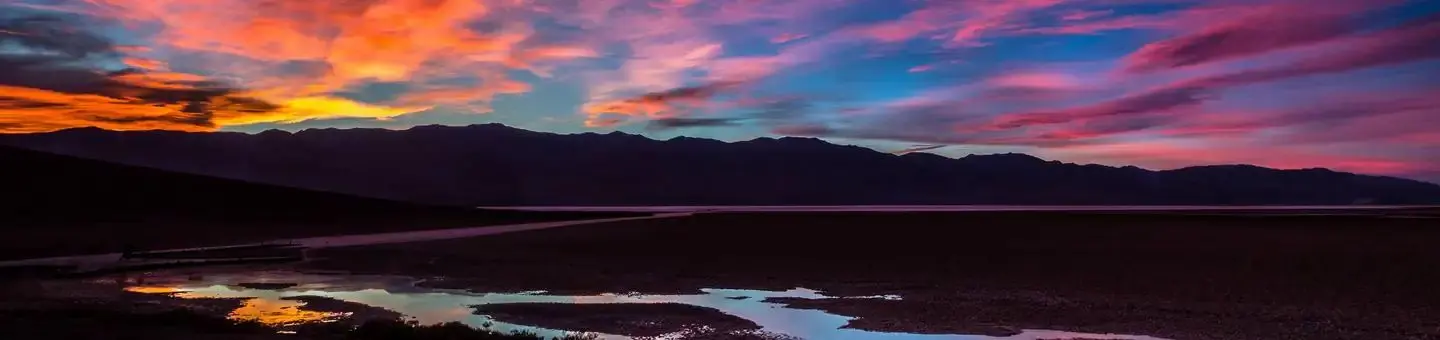 colorful sunset over wide landscape of mountains and small pool of water