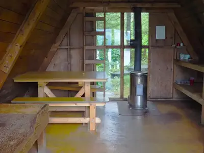Berg Bay Cabin interior with window, wooden ladder, table and oil stove.