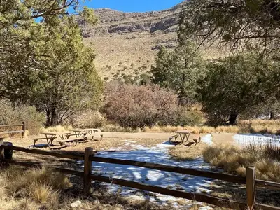 Dog Canyon Group Campsite with two tent pads delineated with landscape timbers and filled with fine crushed gravel. Three picnic tables are located in an open grassy area for groups to gather.