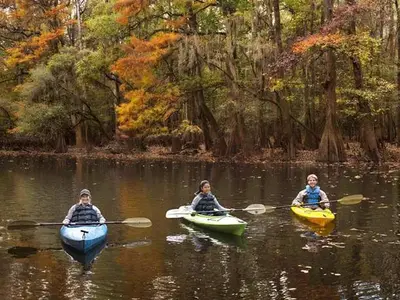 Three children kayak on the water in the autumn