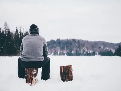 Man sits on log in snow (Unsplash)