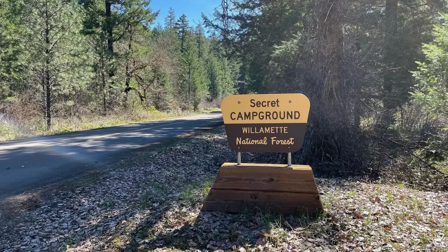 A brown and cream colored plastic sign on a wooden base. The sign reads "Secret Campground".