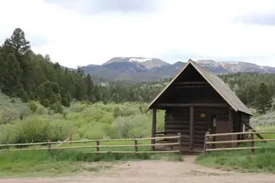 Brown forest service cabin surrounded by green trees and rolling hills