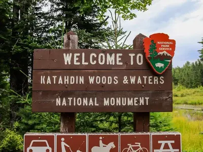 A close up of a National Park welcome sign on the way to Sandbank Stream Campground. It is wooden and says "Welcome to Katahdin Woods and Waters National Monument"