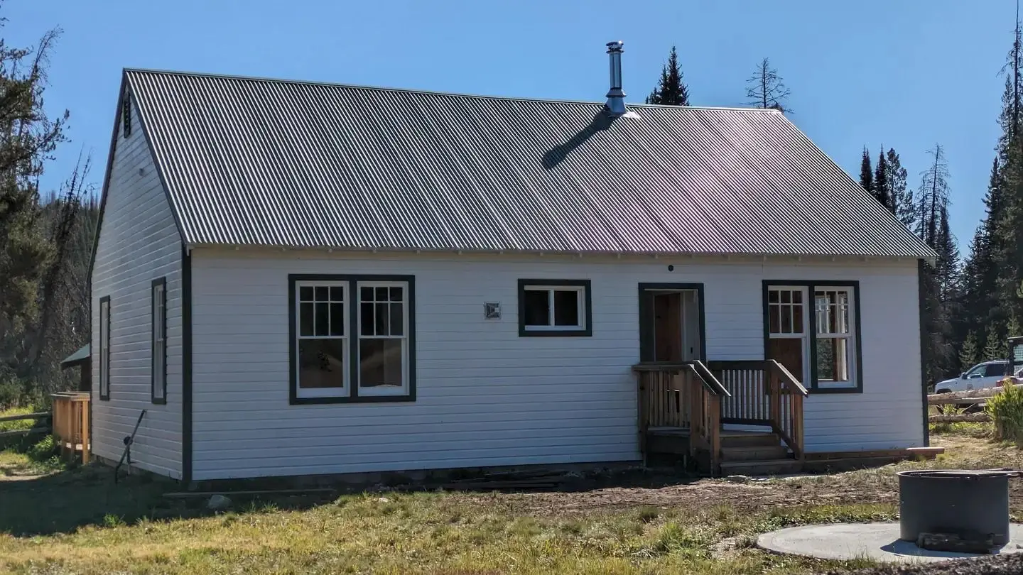 Red painted cabin with white trim and green roof. Fence along the front.