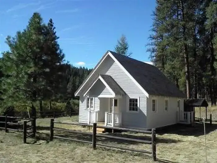 White cabin in meadow with split rail fence and pine trees