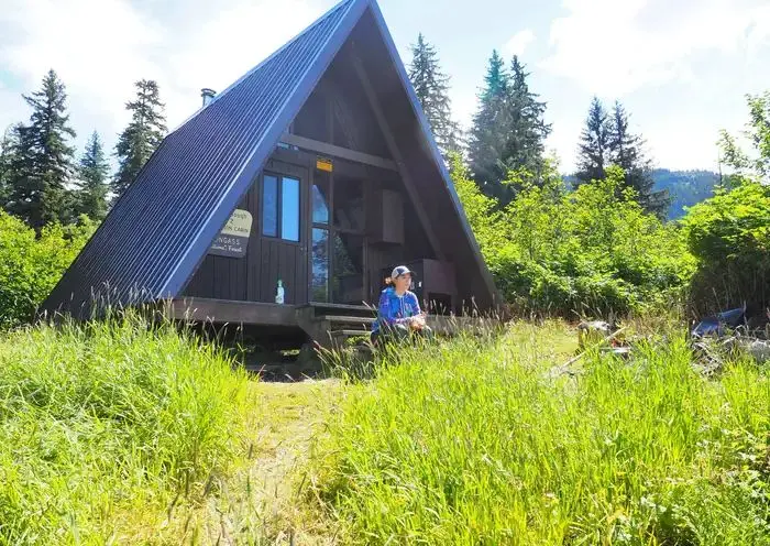 Woman sitting on porch of Shakes Slough 2 Cabin with grass in front and trees in background