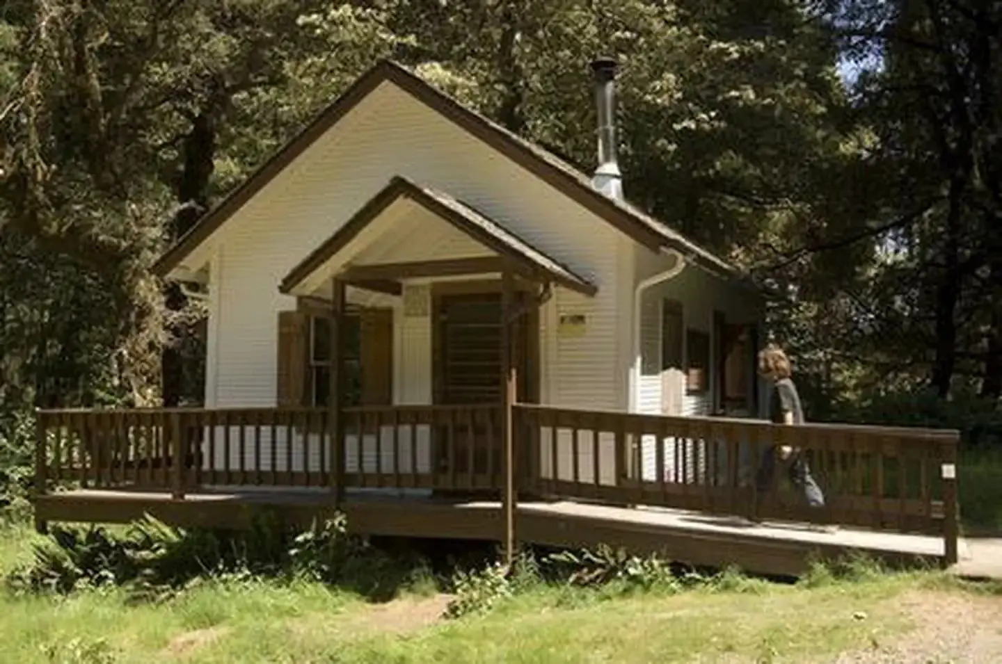 White cabin in the woods with ramp leading to front door and small porch