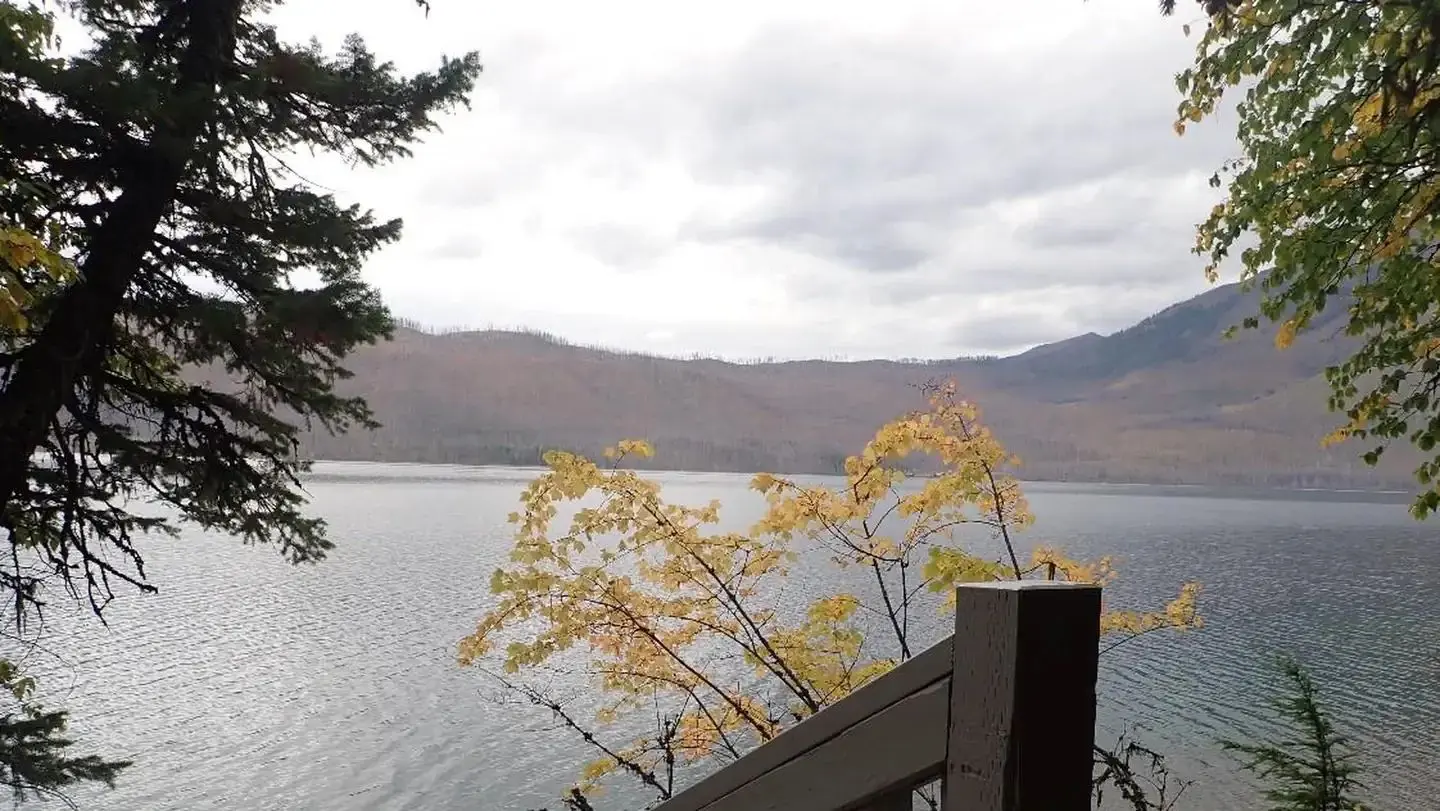 Lake McDonald with fall foliage in the foreground and mountains in the background.