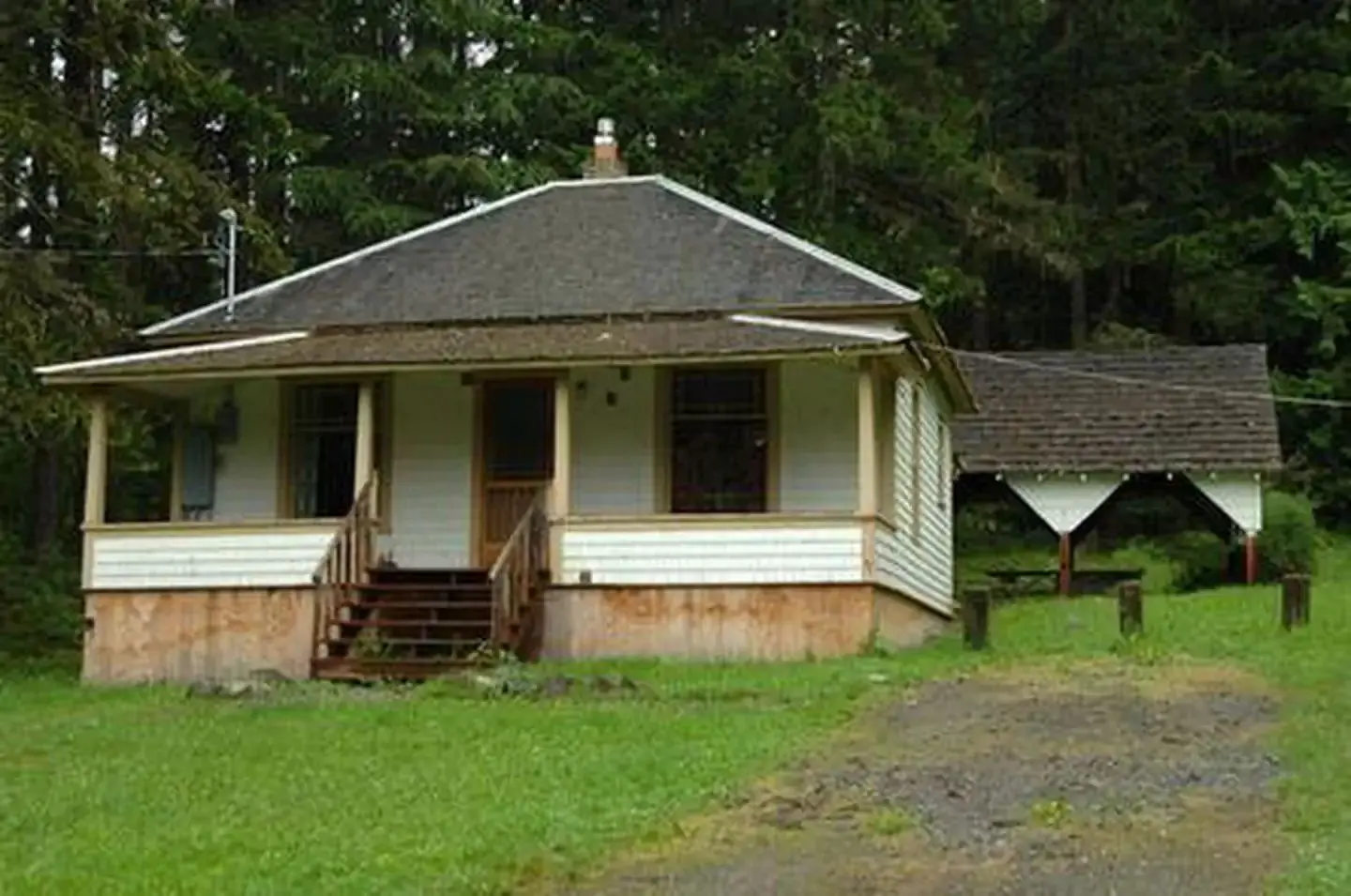 Cabin with front porch in grassy yard in front of forest