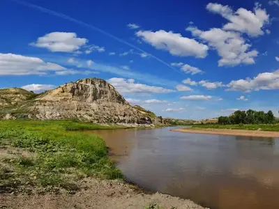 The Little Missouri River flows under a deep blue sky with a dramatic butte in the background