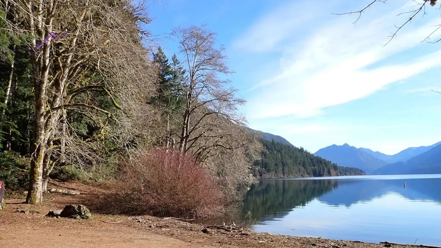 A sunny day in the spring at the Lake Crescent boat launch. Trees line the shores and Mount Storm King can be seen across the lake.