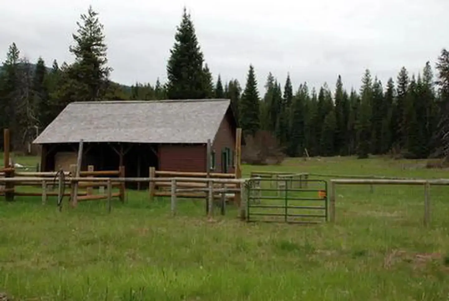 Cabin with red siding and fences in flat meadow backed by conifer forest