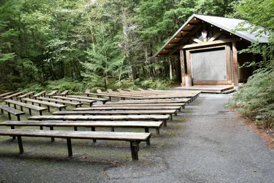 Rustic amphitheater in campground with benches and a building with a stage.