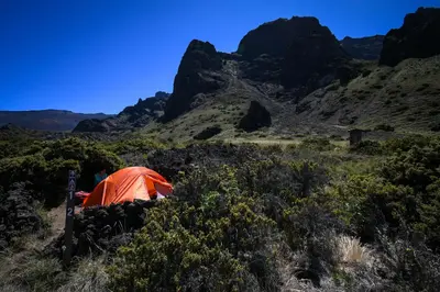 tall cliffs overlook tent site with orange tent and one camper