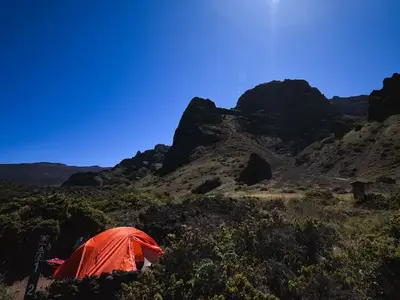 tall cliffs overlook tent site with orange tent and camper