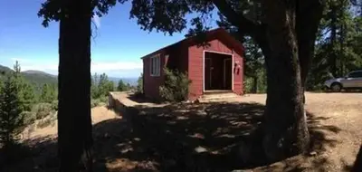 Red cabin in between trees with blue sky in background.
