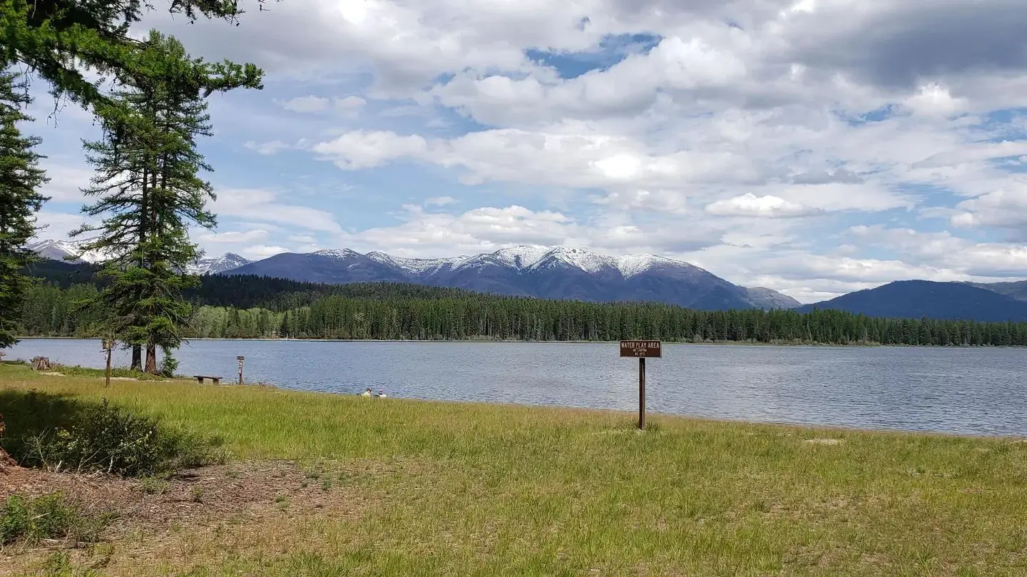 View from swim beach at Seeley Lake Campground, looking east across Seeley Lake. Snow-capped peaks of the Swan Range can be seen in the background.