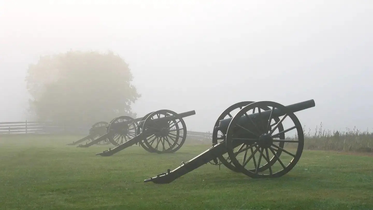 Four civil war cannons along a green foggy field.