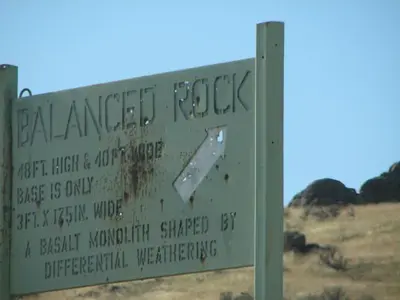 A weathered sign about a weathered Balanced Rock
