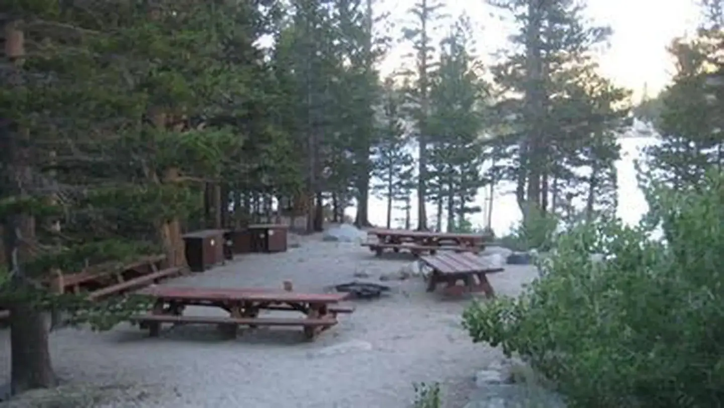 Several picnic tables around a fire ring on a cliff near a lake